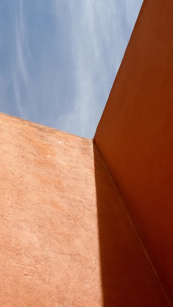 Vista dal basso di un cielo parzialmente nuvoloso e pareti colorate che formano un motivo geometrico.