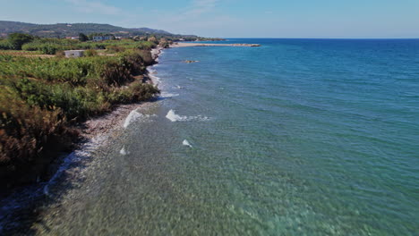 tranquil coast at midday with clear water and gentle waves near a village