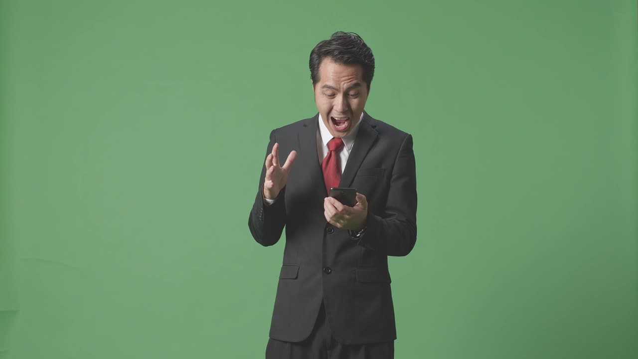 아시아 사업가 한 명 은 휴대 전화 를 사용 하고 스튜디오 에서 녹색 스크린 에 서 있는 동안 와우 라고 말 합니다.