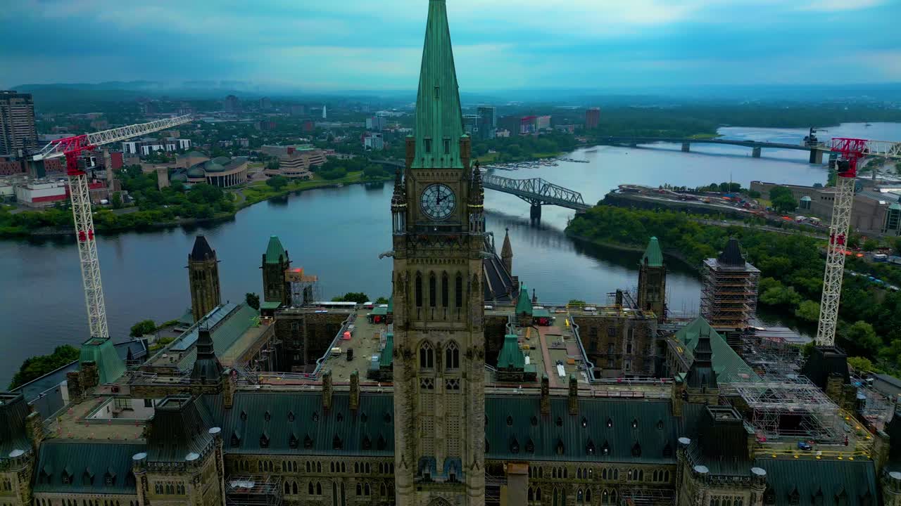 The cloudy sky over Ottawa's Parliament Hill clock tower with the Canadian flag gently waving captured from an aerial drone during renovation work and construction vehicles parked around building T1-2