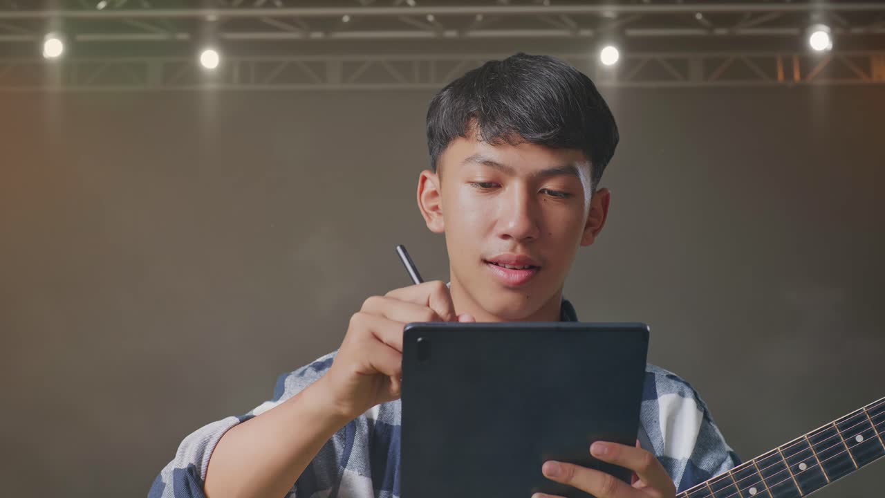 무대 위 에 서 있는 태블릿 에 메모 를 하는 기타 를 들고 있는 아시아 청소년 의 근접 사진