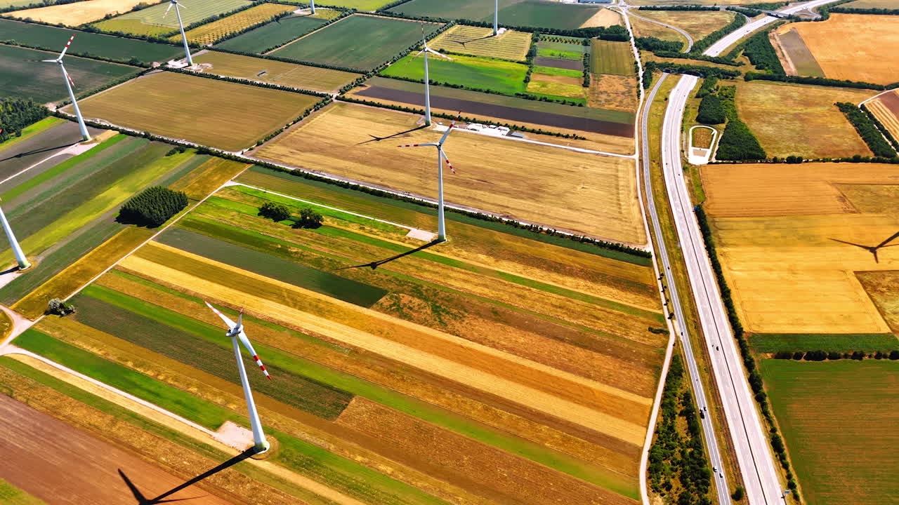 Windmills stand on the colorful fields on sunny day. Production of green energy from the power of wind. Aerial view