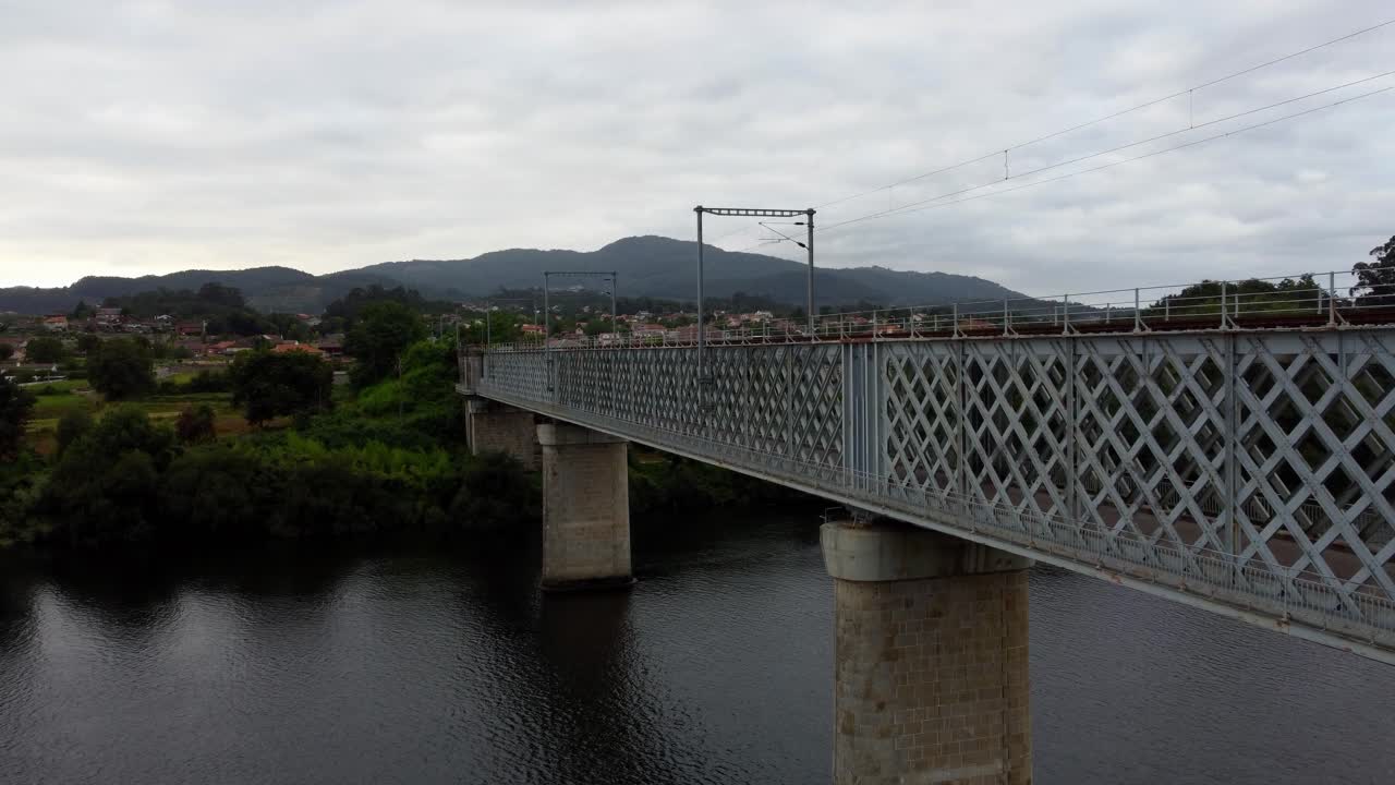 4K drone slow ascent alongside the massive metal railway bridge over the Minho River, connecting the borders of Spain and Portugal, detailing the concrete piers on a cloudy day