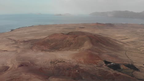 Tirar-Hacia-Atrás-Y-Descender-Disparado-Por-Un-Dron-Detrás-De-Un-Volcán-Rojo-Con-Un-Pequeño-Edificio-Blanco-En-La-Parte-Superior