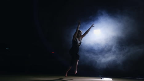 Young-woman-gymnast-runs-up-and-performs-a-front-flip-and-screw-in-the-air-in-slow-motion-in-the-gym-on-the-carpet-in-the-smoke-Steadicam