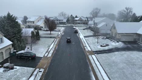 aerial tracking shot of car driving through snow covered neighborhood during snow flurries in winter