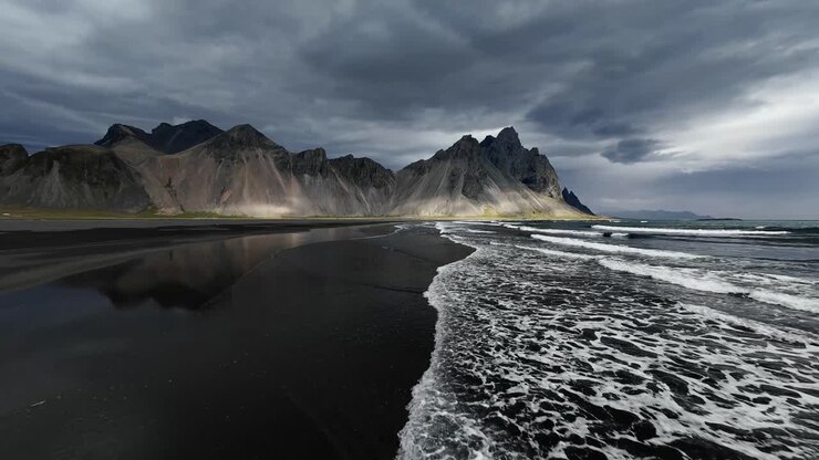 Un volo cinematografico con drone FPV sopra la perfetta spiaggia di sabbia nera di Stokksnes, Islanda, che vola direttamente verso le spettacolari cime del monte Vestrahorn