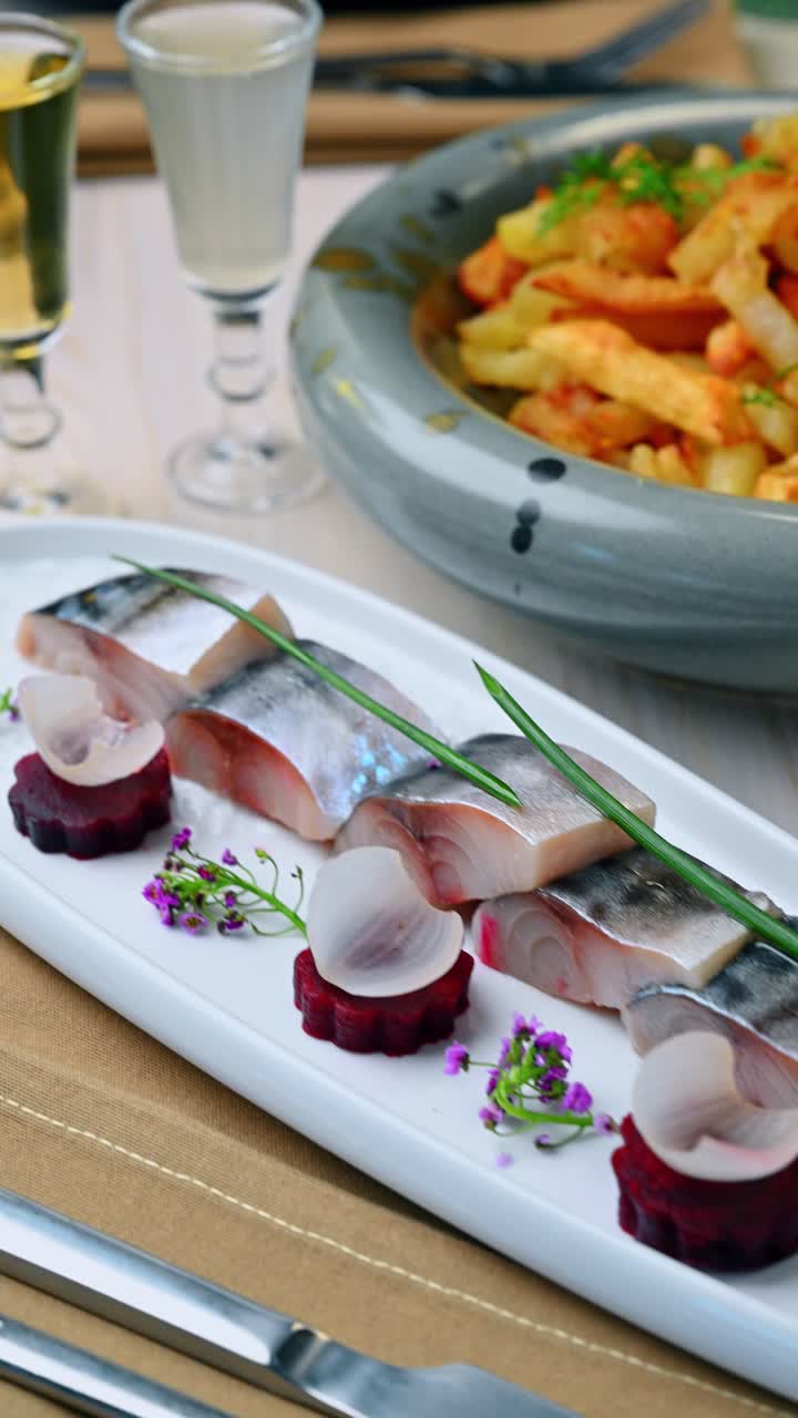 Antipasto di pesce salato con barbabietola e superalcolici sul tavolo. Primo piano di fette di aringa con guarnizione e due bicchierini di diverse bevande alcoliche sullo sfondo