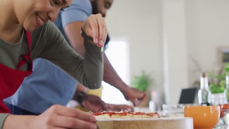 Smiling-diverse-female-and-male-friends-making-pizza-and-cooking-in-kitchen,-in-slow-motion