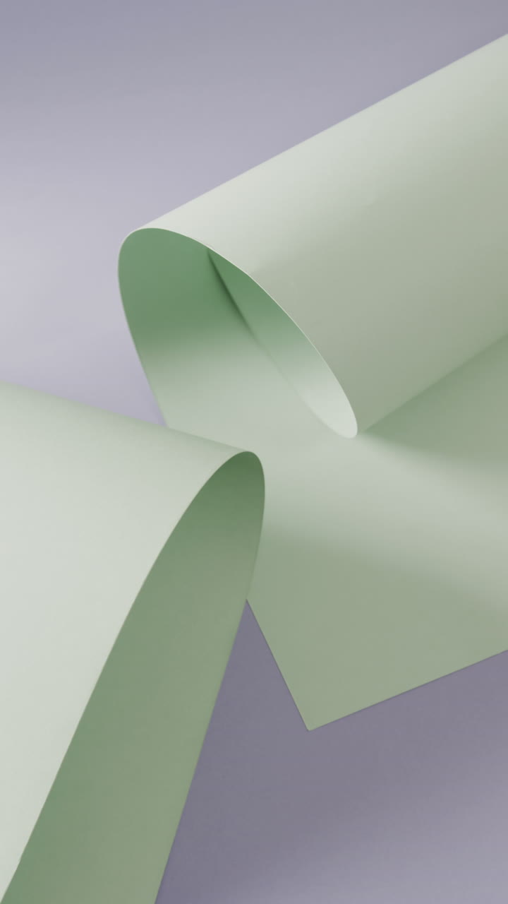 Vertical video of close up of pale green rolled pieces of paper on blue background with copy space