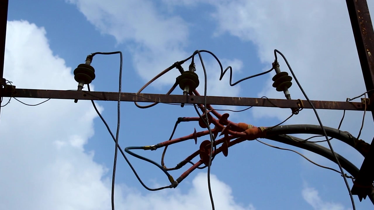 Slow zoom footage of overhead electrical distribution lines, insulators, and utility hardware against blue sky. Ideal for energy, electricity supply, infrastructure, and power grid projects.
