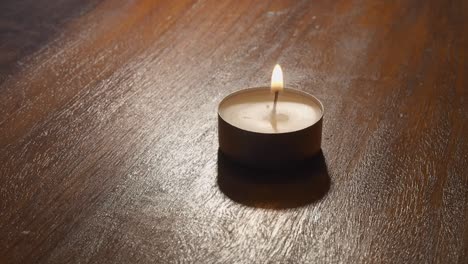 close up: lighter flame used to light paraffin tea candle on table top