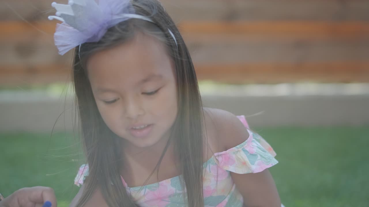 엄마와 어린 딸이 뒷마당에서 담요 위에 앉아 함께 그림을 그리고 있습니다. 야외 장면은 평화로운 가족 순간을 포착하여 창의성과 유대를 촉진합니다.