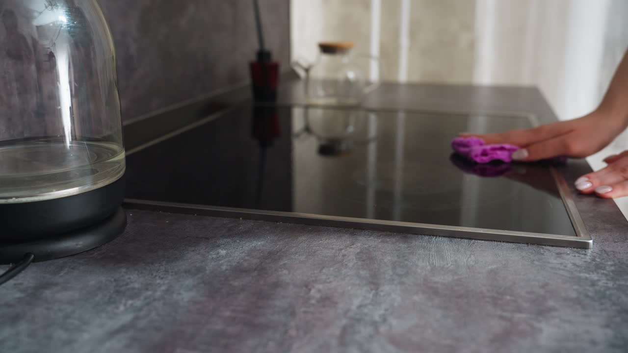 Caucasian Cook Wiping Glass Stove Surface Steady Hand Moves Microfiber Across Induction Glass, Steam Traces And Grease Removed, Ecoconscious Homemaker Restoring Shine After Meal, Warm Natural Light