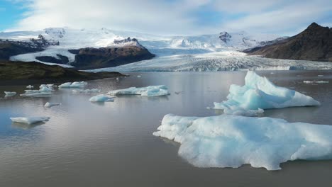drone pasando por pequeños glaciares flotando en un lago en islandia durante el invierno