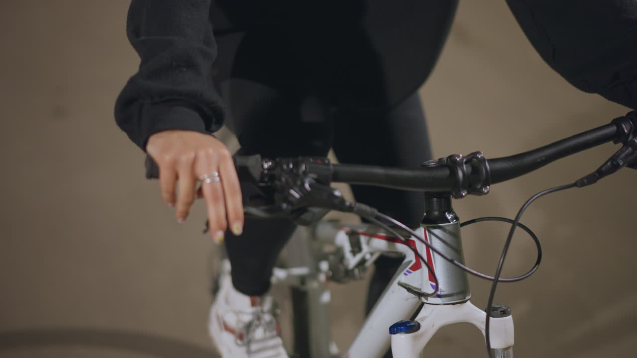 Closeup Hands Gripping Bicycle Handlebar, Rider Steadying Bike With Visible Ring And Hoodie Sleeve, Tactile Focus On Brake Lever And Cables, Studio Like Neutral Background, Deliberate Control