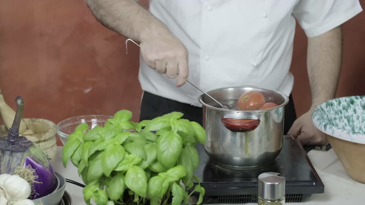 el cocinero usa un desnatador para sacar los tomates hervidos de la olla de agua caliente y colocarlos para que se enfríen en un cuenco de vidrio