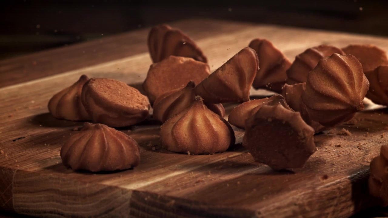 Golden Brown Cookies Falling onto a Wooden Cutting Board in Slow Motion