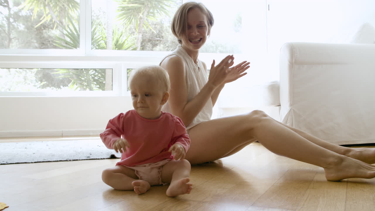 madre feliz apretando las manos, jugando con el bebé y sentada en el suelo
