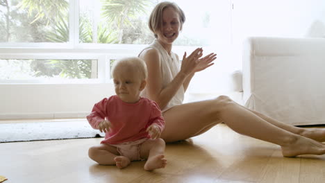 happy mom clasping hands, playing with baby and sitting on floor