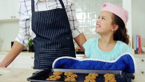 Smiling-girl-keeping-tray-of-fresh-cookies-on-worktop