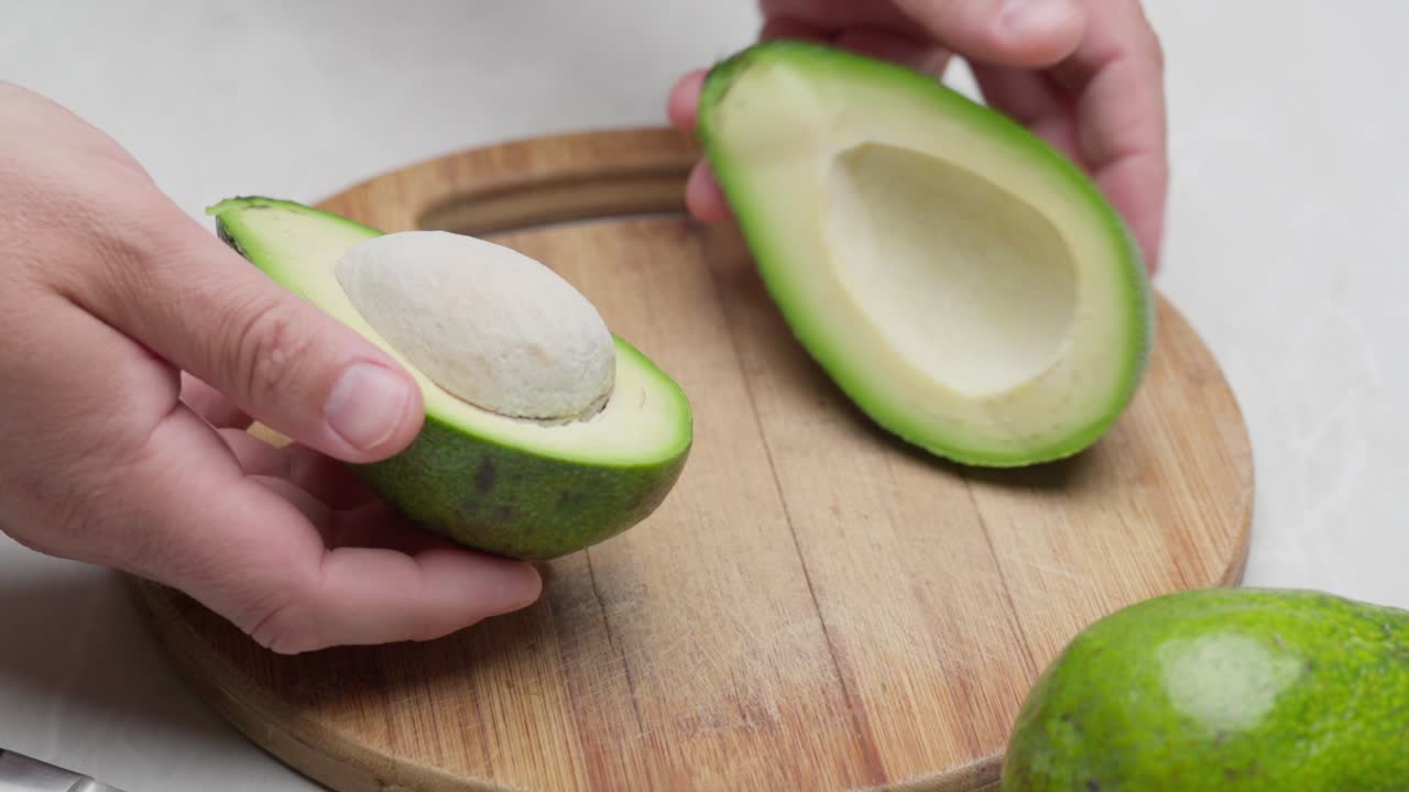 Primo piano di un avocado tagliato a metà e denocciolato con un coltello su una tavola di legno