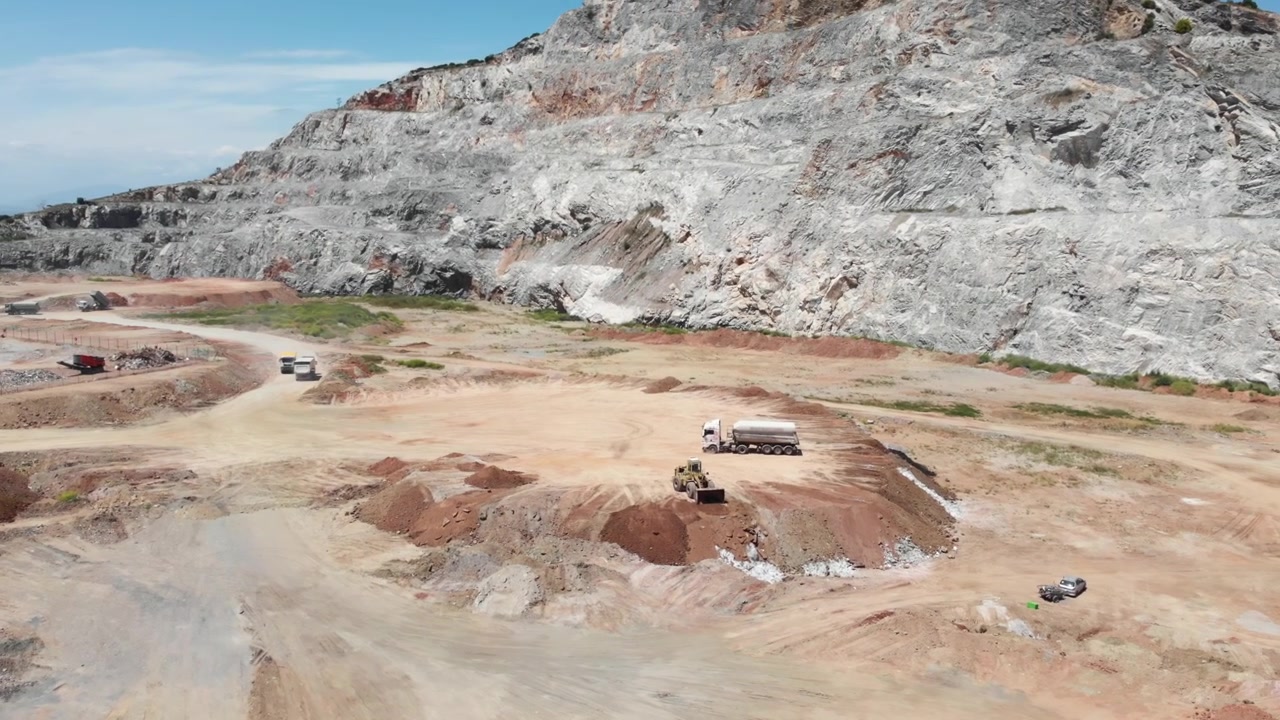 Máquinas pesadas e caminhões manobram por uma grande pedreira com formações rochosas visíveis. Ideal para projetos com tema industrial e de construção