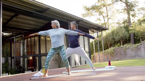 una pareja de ancianos concentrados practicando yoga en el jardín.