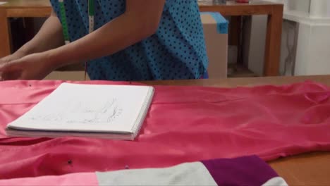 diseñador de moda latino tomando medidas de un vestido en una mesa de madera escribiendo notas