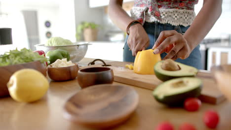 a young african american woman is slicing yellow pepper in a kitchen, at home
