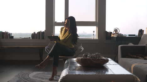 young businesswoman writing on her digital tablet in her nice penthouse living room above the city life