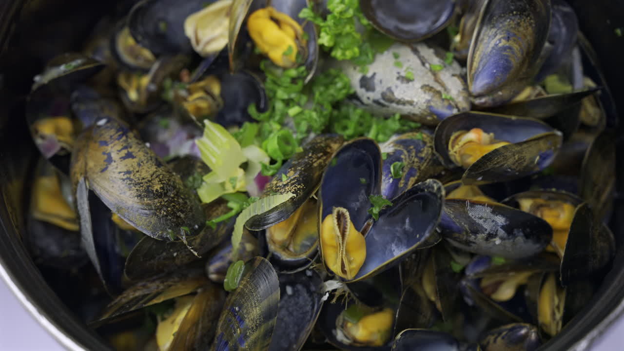 Close up of multiple steamy mussels in a pot with green onions on top