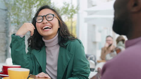 joyous asian woman chatting with african american man in outdoor cafe