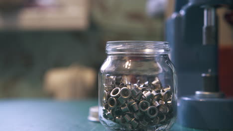 different silver eyelet parts lie in transparent jar closeup