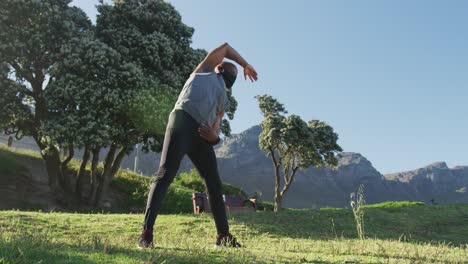 senior african american man wearing face mask exercising stretching in countryside