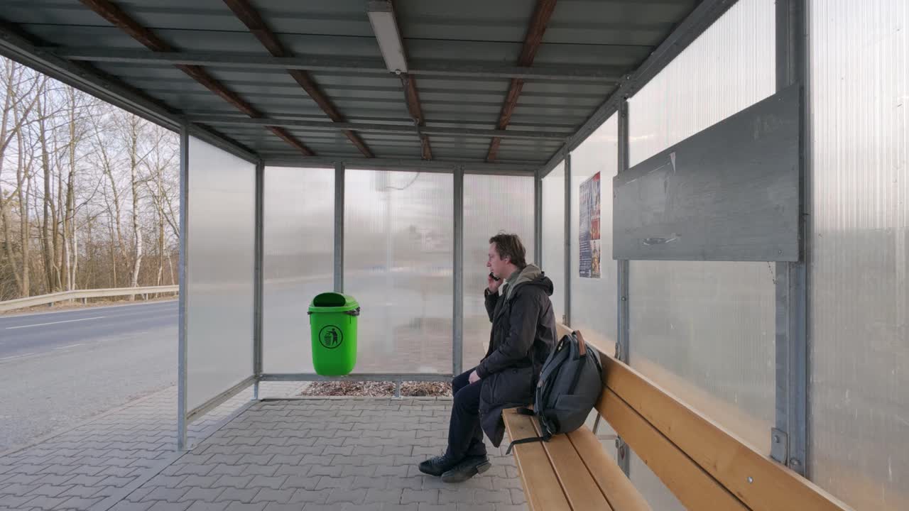 Un uomo in attesa alla fermata dell'autobus compone un numero e parla al telefono. Passare il tempo con la tecnologia moderna.