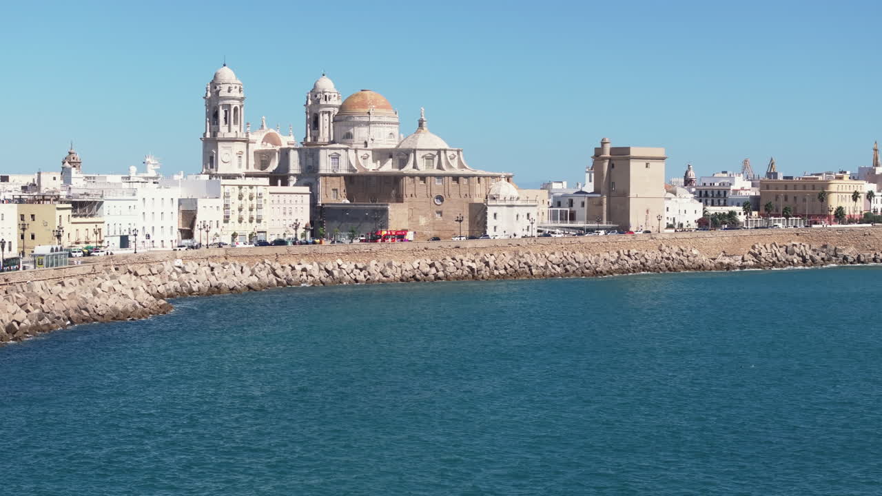 Ripresa aerea cinematografica con drone di Cadice, Andalusia, Spagna, in una giornata di sole, che mostra la Cattedrale di Cadice e lo storico lungomare mentre il drone vola in avanti. Color grading cinematografico