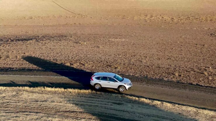 Ripresa in movimento con drone di un'auto che si dirige verso la telecamera lungo una stretta strada sterrata tra campi dorati all'alba
