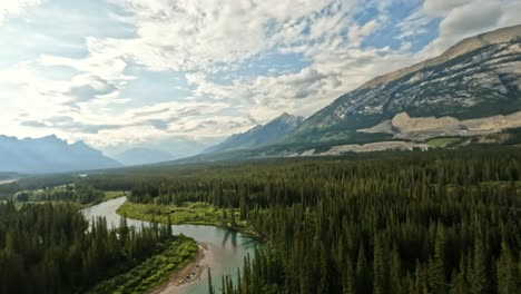 fpv drone begins at the bow river, skimming over shimmering waters and scattered stones. it ascends gracefully, unveiling lush spruce trees, the glowing sunlit sky, and the expansive valley landscape