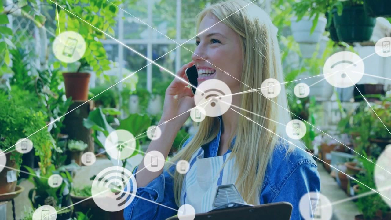 Donna in un vivaio che risponde a una telefonata e controlla gli appunti, mentre una sovrapposizione grafica di rete si estende sulle piante e su di lei.