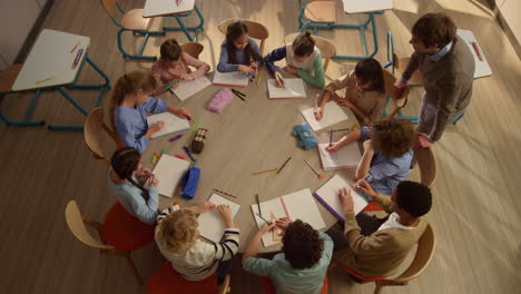 schoolchildren having lesson at round table. male teacher helping kids at lesson