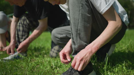 close-up of a grandfather and his two grandsons focusing intently as they tie their shoelaces on a grassy field