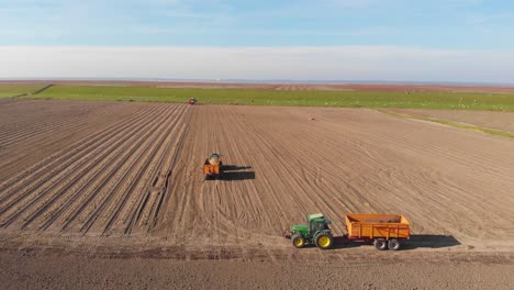 drone shot of tractors, farmers working on brown, earthy farmland, plowing and harvesting