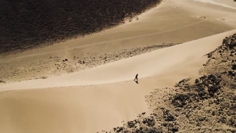 man walks up ridge of a high sand dune in hot desert