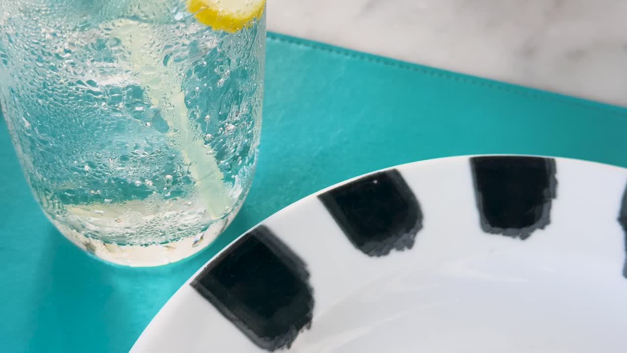 레몬이 있는 클럽 소다 한 잔이 패턴이 있는 접시 의 활기찬 푸른색 테이블에 앉아서 상쾌한 식사 장면을 촬영합니다.