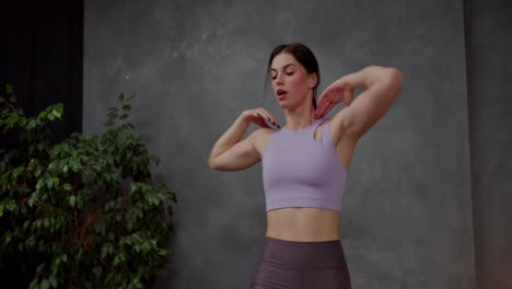 confiada chica atlética morena en una camiseta deportiva púrpura hace deportes y levanta las rodillas a los codos en un apartamento moderno cerca de una gran planta interior