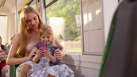 Niña-Con-Madre-Usando-La-Aplicación-De-Red-Social-De-Internet-De-Teléfono-Móvil-Mientras-Viaja-En-Autobús