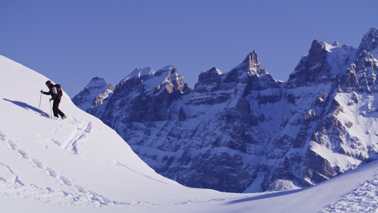Freeride skier skinning up with Dents du Midi backdrop, then charging steep powder on a bluebird day near Champéry and Avoriaz.