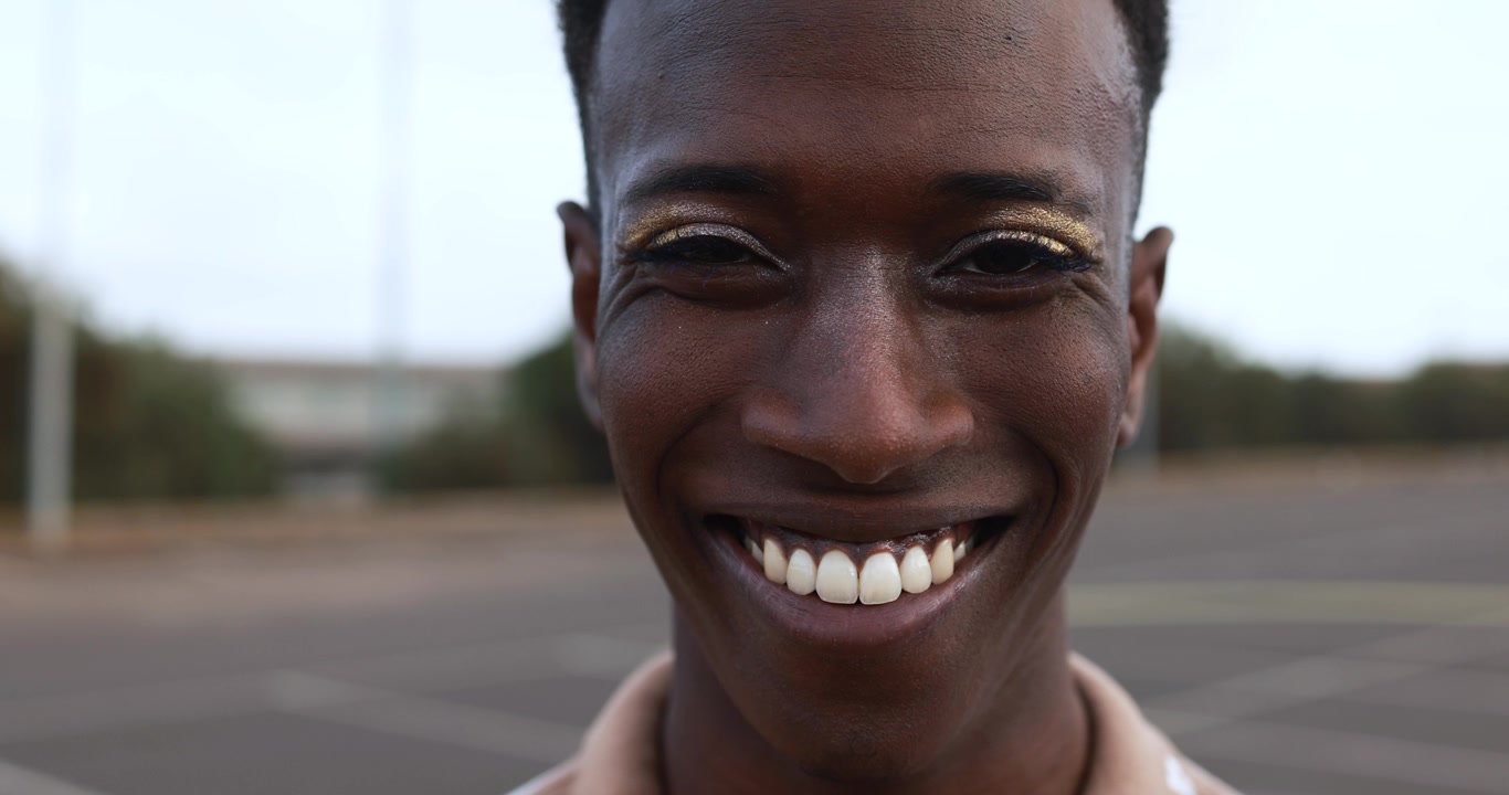 Close-up de um jovem negro com sombra com glitter sorrindo alegremente