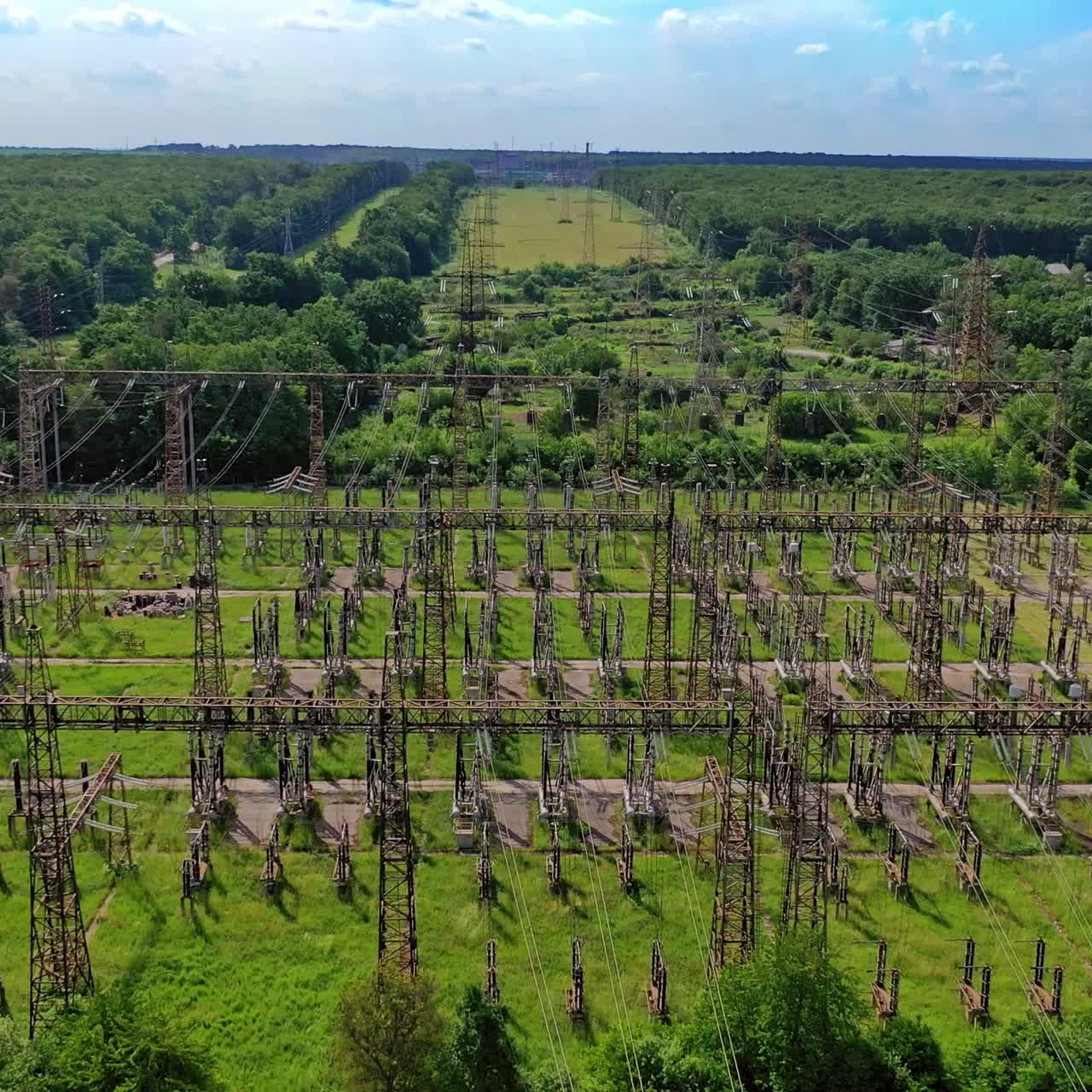 High voltage steel pylons in green field. View from above the power transmission lines. Electric tower line among nature. Aerial view.